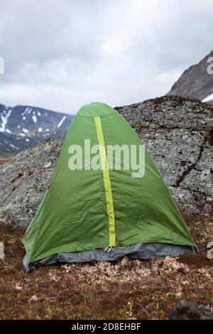 Verde impermeabile e vento tenda per escursioni è in montagna a tempo ventoso, si trova dietro grande pietra per la protezione dal vento Foto Stock