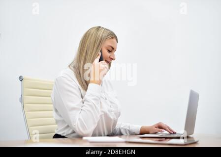 Giovane manager bianco caucasico donna che parla di smartphone e di lavoro con computer portatile in ufficio Foto Stock