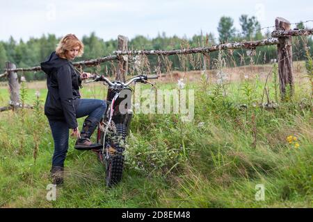 Il cavaliere femmina maturo stringe i suoi stivali per cavalcare moto sporco in campagna, copyspace Foto Stock