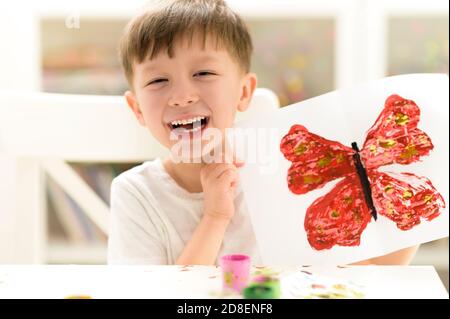 Orgogliosa kid che mostra la sua vernice buterfly imbarcazione a kindergarten Foto Stock
