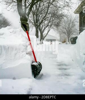 Una pala con manico rosso ciliegia arroccata contro 4 piedi di neve che si snoda lungo un marciapiede a Chicago durante una bizzard di gennaio. Foto Stock