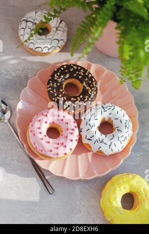 Dolci e fresche ciambelle diverse colorate con cioccolato smerigliato, smaltato e spruzzato, glassatura su piastra rosa su fondo di cemento. Foto Stock