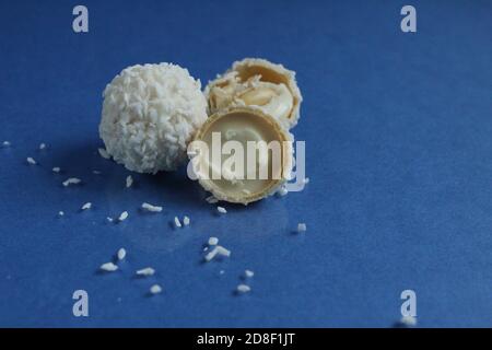 tre bianchi con caramelle al cocco e metà con waffle E crema bianca come Raffaello su sfondo blu e luminoso con spazio di copia per il testo Foto Stock