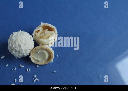 tre bianchi con caramelle al cocco e metà con waffle E crema bianca come Raffaello su sfondo blu e luminoso con spazio di copia per il testo Foto Stock