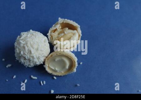 tre bianchi con caramelle al cocco e metà con waffle E crema bianca come Raffaello su sfondo blu e luminoso con spazio di copia per il testo Foto Stock