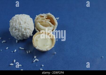 tre bianchi con caramelle al cocco e metà con waffle E crema bianca come Raffaello su sfondo blu e luminoso con spazio di copia per il testo Foto Stock