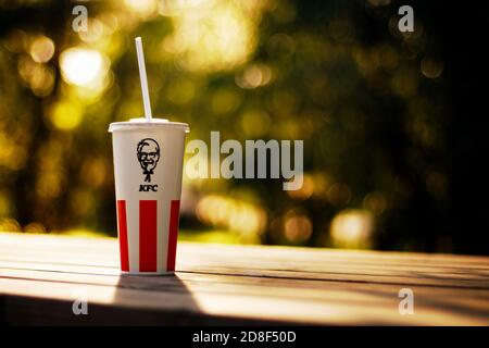 Tazza di carta con logo KFC su sfondo di alberi sfocati all'aperto Foto Stock