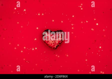 Composizione natalizia o di San Valentino realizzata con decorazione a cuore glitterig e glitter su superficie rossa. Buon natale e felice anno nuovo 2021, felice Foto Stock