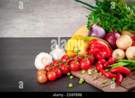 Cibo sfondo su tavola di legno nero. Ingredienti per cucinare cibo - pomodori ciliegini, cipolle, patate, peperoni rossi e gialli, piselli in cialda e gar Foto Stock