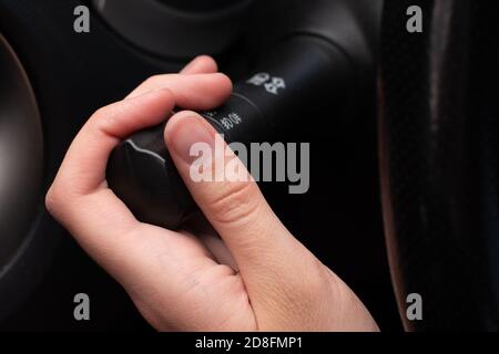 Close-up la mano femmina attiva la leva degli indicatori di direzione, accende l'illuminazione e la messa a fuoco selettiva. Sicurezza stradale Foto Stock