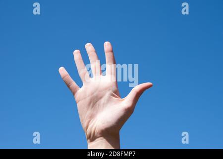 Closeup gesto di una mano di una donna che mostra cinque dita, isolato contro un cielo blu, lingua del segno simbolo numero cinque Foto Stock
