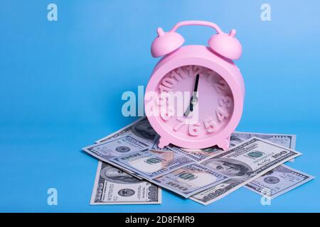 sveglia rosa, banconote su sfondo blu. concetto di business femminile. Lavorare mentre dormono Foto Stock