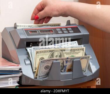 Donna cassiere che mette cento dollari banconote americane in valuta banco alla cassa Foto Stock