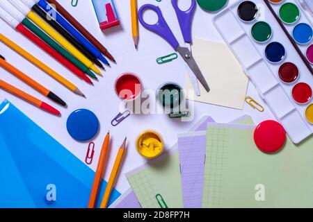 La cancelleria per la scuola è su uno sfondo bianco. Penne, matite, pitture, una piegatrice, taccuini, graffette, magneti Foto Stock