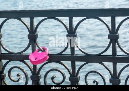 Lucchetto rosa a forma di cuore sul bordo di metallo forgiato del ponte sul fiume. Simbolo di amore e fedeltà degli sposi novelli. Tradizione nuziale. Foto Stock