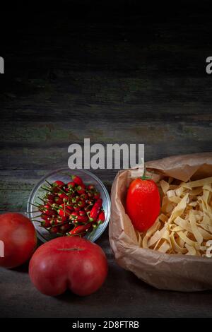 Foto di Tagliatelle con peperoni rossi e pomodori Su sfondo di legno scuro decaduto Foto Stock