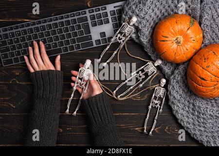 Le mani femminili e le decorazioni di Halloween con scheletro e computer portatile su tavolo di legno scuro. Vista dall'alto, disposizione piatta. Concetto di fondo del festival Foto Stock