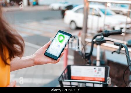Navigazione in Internet. Una donna tiene in mano uno smartphone con una mappa online. Sullo sfondo, una bicicletta e una strada sono sfocate. Primo piano della mano. Foto Stock