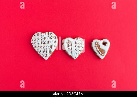 Tre biscotti gingersnap sotto forma di cuore su sfondo rosso, vista dall'alto, spazio per la copia Foto Stock