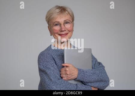 Donna matura che indossa occhiali che tengono un computer portatile e sorridente. Foto Stock