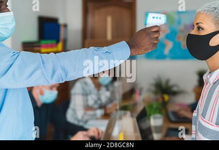 I giovani in collaborazione con lo spazio creativo, controllo della temperatura con il digitale termometro indossando la maschera facciale e mantenendo la distanza sociale Foto Stock