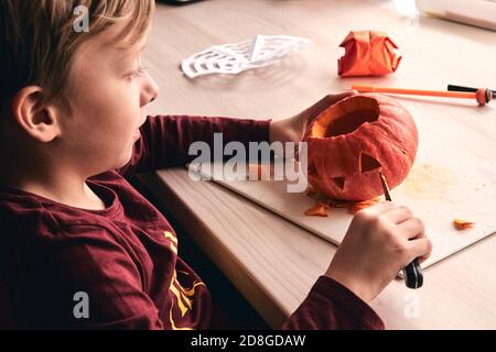 Halloween, decorazione e idee di vacanza - primo piano di capretto con la zucca di intaglio del coltello o jack-o-lanterna. il ragazzo di 6 anni ha attività di divertimento casalinga. Mamma Foto Stock