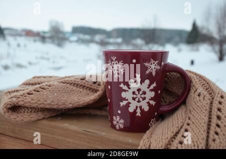 Coppa rossa o borgogna con un modello di fiocchi di neve sullo sfondo di una foresta invernale. Nevicare. Capodanno. Natale. Tazza con una bevanda calda sul Foto Stock