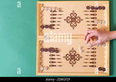 La mano tiene un chip bianco per la mossa successiva, un gioco di backgammon. Concetto di vittoria Foto Stock