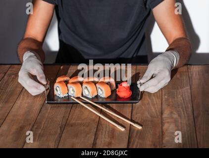 Le mani in guanti di gomma servono il sushi su un tavolo di legno. Menu sushi. Foto Stock