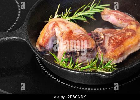 Costolette di lombo di agnello con rosmarino in una padella in ghisa. Cucinare su un fornello elettrico Foto Stock