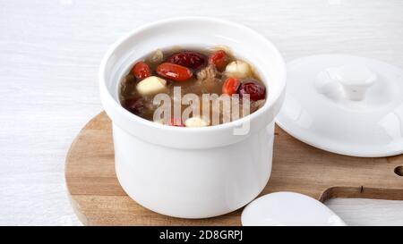 Primo piano della tradizionale zuppa cinese di funghi bianchi e dolci con semi di loto, datteri rossi (jujibe) e mirtillo (goji, gogyberry) su sfondo bianco. Foto Stock