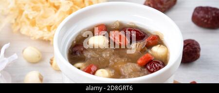 Primo piano della tradizionale zuppa cinese di funghi bianchi e dolci con semi di loto, datteri rossi (jujibe) e mirtillo (goji, gogyberry) su sfondo bianco. Foto Stock