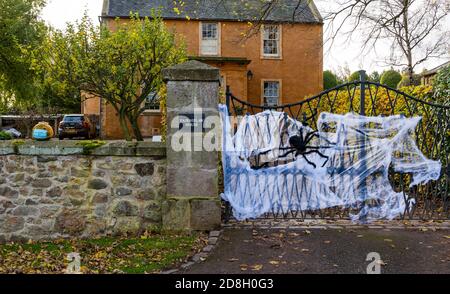 East Lothian, Scozia, Regno Unito, 30 ottobre 2020. Decorazioni di Halloween: Una casa in Athelstaneford entra nello spirito di Halloween decorando una porta con un grande web di ragno e ragno falso così come le zucche su una parete, uno che indossa una maschera facciale Foto Stock