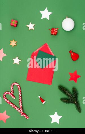 vista dall'alto della busta rossa con il biglietto vicino ai baubles di natale, stelle cotte al forno e canne caramelle sul verde Foto Stock