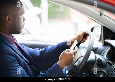 Distratto African Man Texting sul cellulare durante la guida Foto Stock