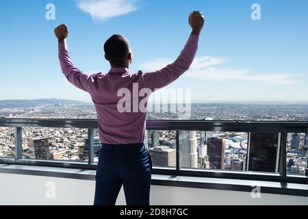 Uomo d'affari africano alzando le mani. Vista posteriore vicino alla finestra con il centro città Foto Stock