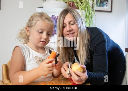 Una madre e una figlia di tre anni che pelano insieme le verdure Foto Stock