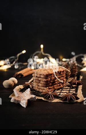 speculaius accatastato con nastro di imballaggio avvolto su una griglia di raffreddamento nera, decorato con stelle di legno, bastoncini di cannella e stelle di anice, sullo sfondo Foto Stock