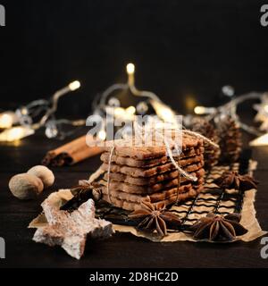 speculaius accatastato con nastro di imballaggio avvolto su una griglia di raffreddamento nera, decorato con stelle di legno, bastoncini di cannella e stelle di anice, sullo sfondo Foto Stock