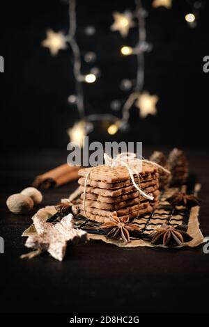 speculaius accatastato con nastro di imballaggio avvolto su una griglia di raffreddamento nera, decorato con stelle di legno, bastoncini di cannella e stelle di anice, sullo sfondo Foto Stock