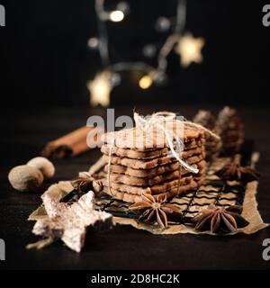 speculaius accatastato con nastro di imballaggio avvolto su una griglia di raffreddamento nera, decorato con stelle di legno, bastoncini di cannella e stelle di anice, sullo sfondo Foto Stock