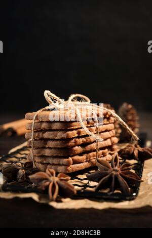 speculaius accatastato con nastro di imballaggio avvolto su una griglia di raffreddamento nera, decorato con stelle di legno, bastoncini di cannella e stelle di anice, sullo sfondo Foto Stock