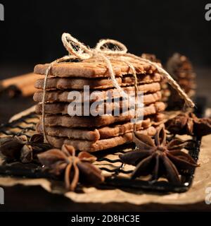 speculaius accatastato con nastro di imballaggio avvolto su una griglia di raffreddamento nera, decorato con stelle di legno, bastoncini di cannella e stelle di anice, sullo sfondo Foto Stock