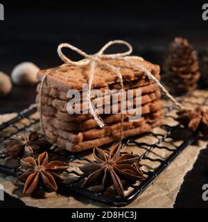 speculaius accatastato con nastro di imballaggio avvolto su una griglia di raffreddamento nera, decorato con stelle di legno, bastoncini di cannella e stelle di anice, sullo sfondo Foto Stock