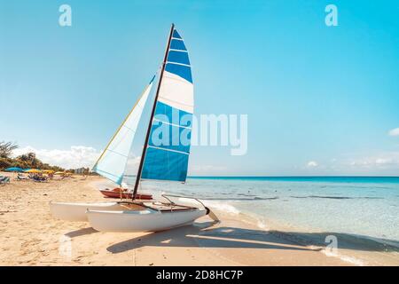 Il catamarano a vela è parcheggiato sulla sabbia bianca della riva sullo sfondo di una splendida natura tropicale. Attrazioni turistiche a Cuba. Foto Stock