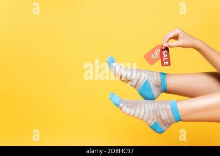 Vista tagliata di donna che indossa calze a righe, tenendo tag con simbolo del dollaro e parola di vendita isolato sul giallo Foto Stock