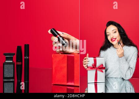 collage di donna che prende il rossetto dalla scatola del regalo vicino decorativo cosmetici sul rosso Foto Stock