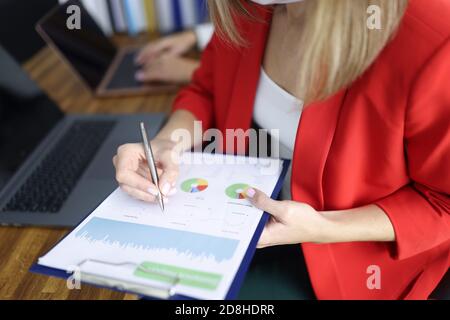 Donna in giacca rossa insegni documento sulla clipboard un tavolo con un collega in primo piano in ufficio Foto Stock