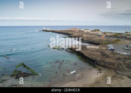 I beachgoers giocano in acqua vicino al faro di Praia a Santiago, Cabo Verde. Foto Stock