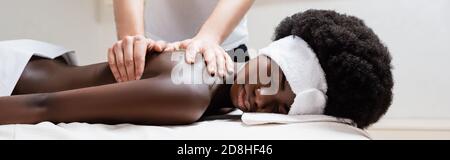 Massaggiatore donna afroamericana con fascia bianca in salone termale, striscione Foto Stock